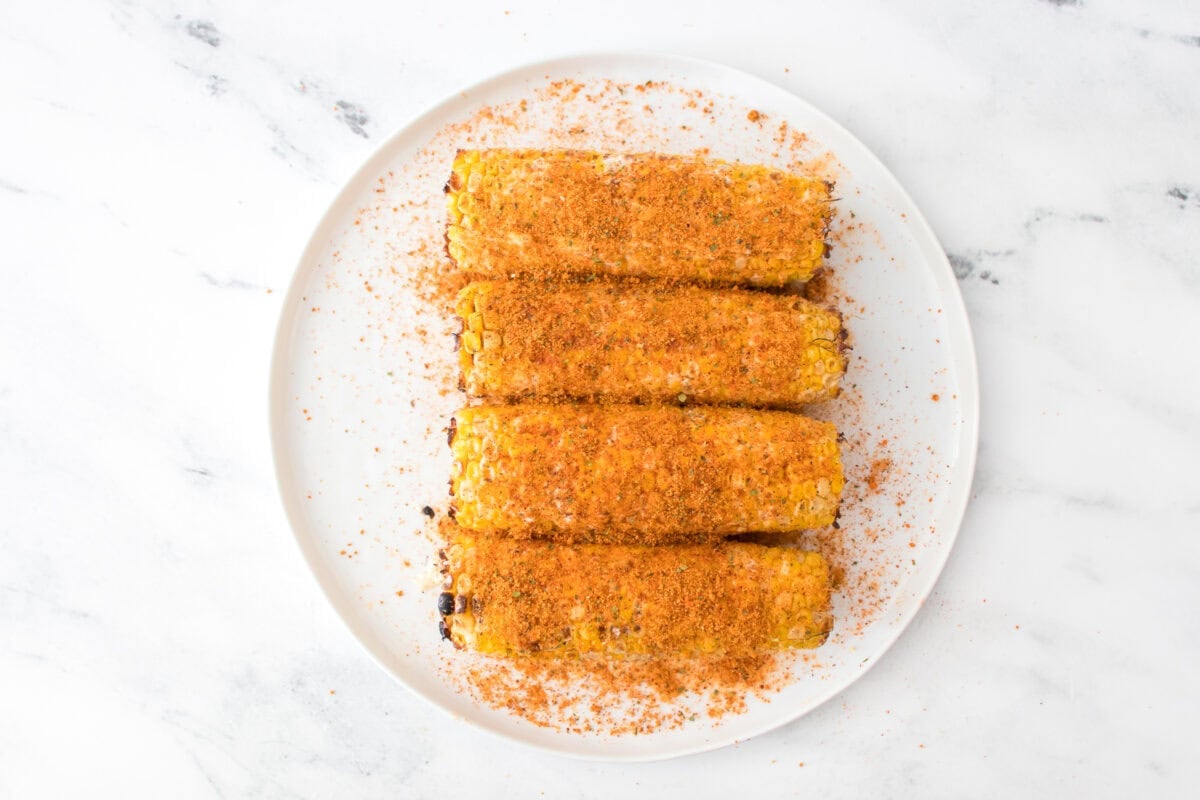 grilled corn that's been coated with mayo, lime juice and elote seasoning on white plate