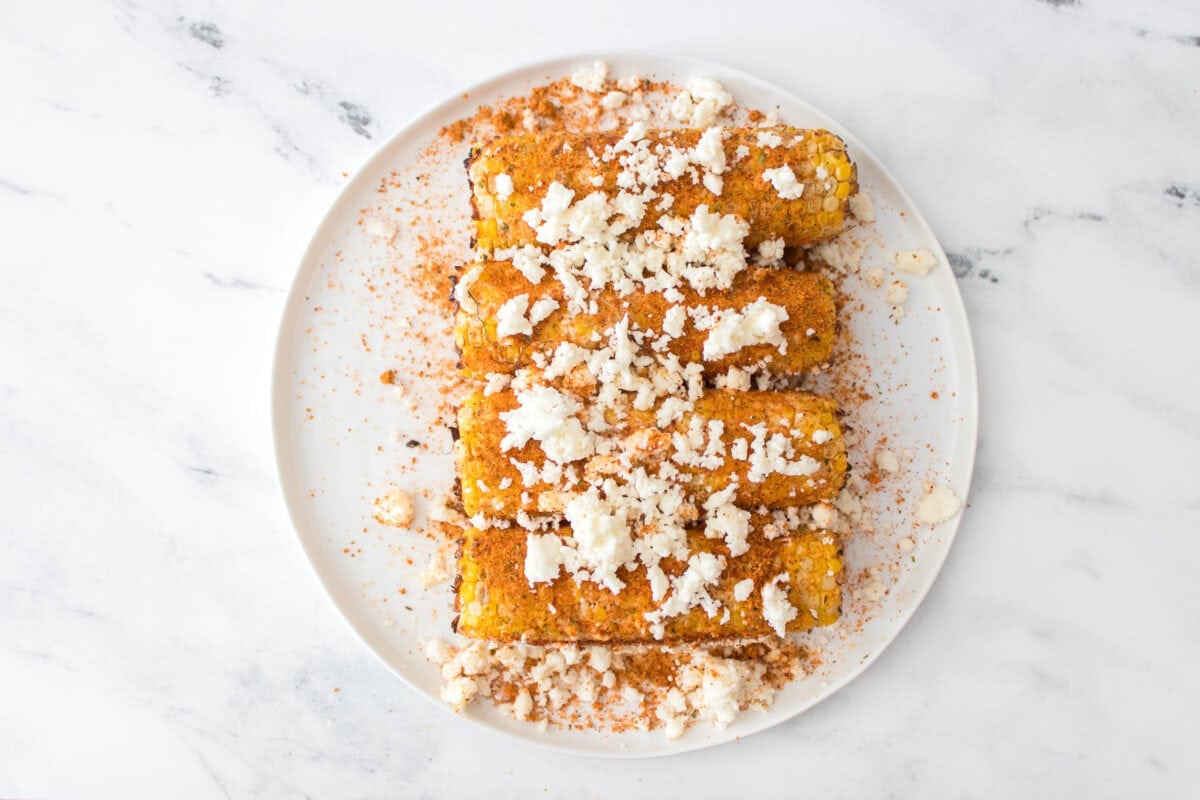 grilled corn that's been coated with mayo, lime juice, elote seasoning and cojita cheese on white plate