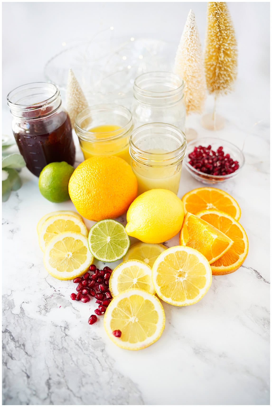 jars of orange juice, pomegranate juice, lime juice, sparkling water, citrus rounds and pomegranate arils