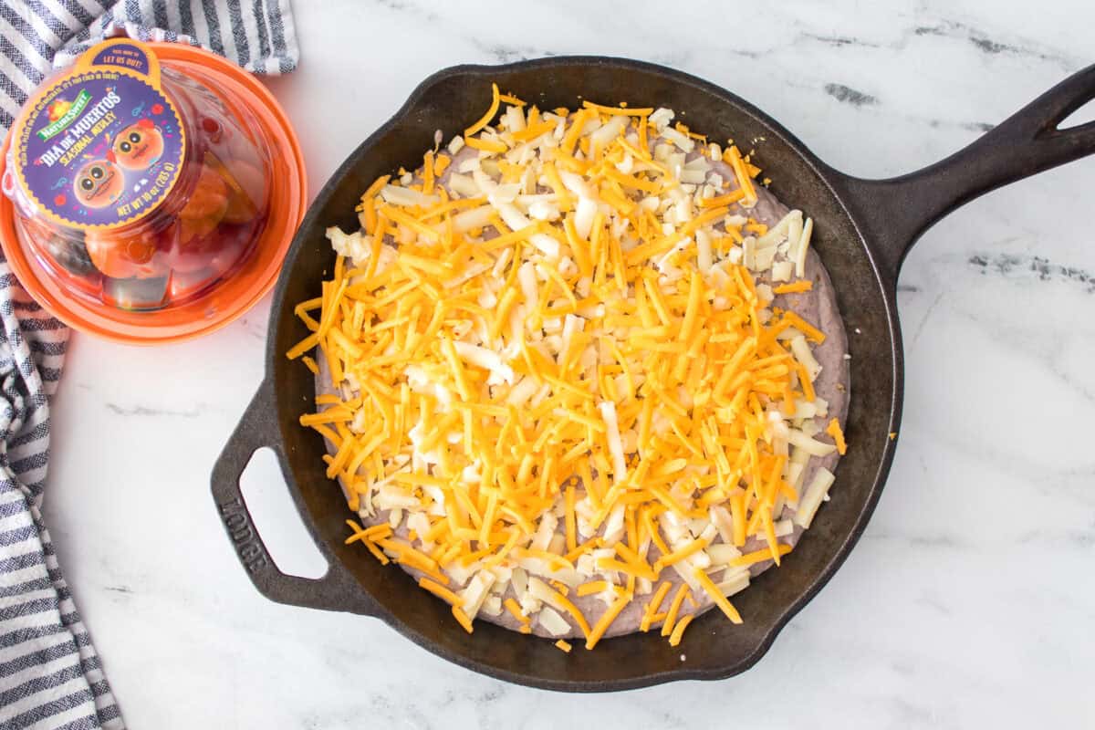 overhead shot of black bean dip before baking in cast iron skillet topped with shredded pepper jack and cheddar cheese