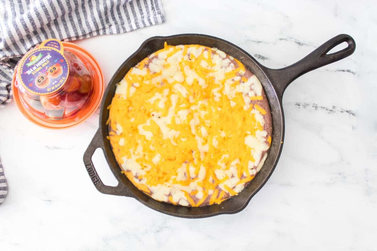 overhead shot of black bean dip after baking in cast iron skillet topped with shredded pepper jack and cheddar cheese