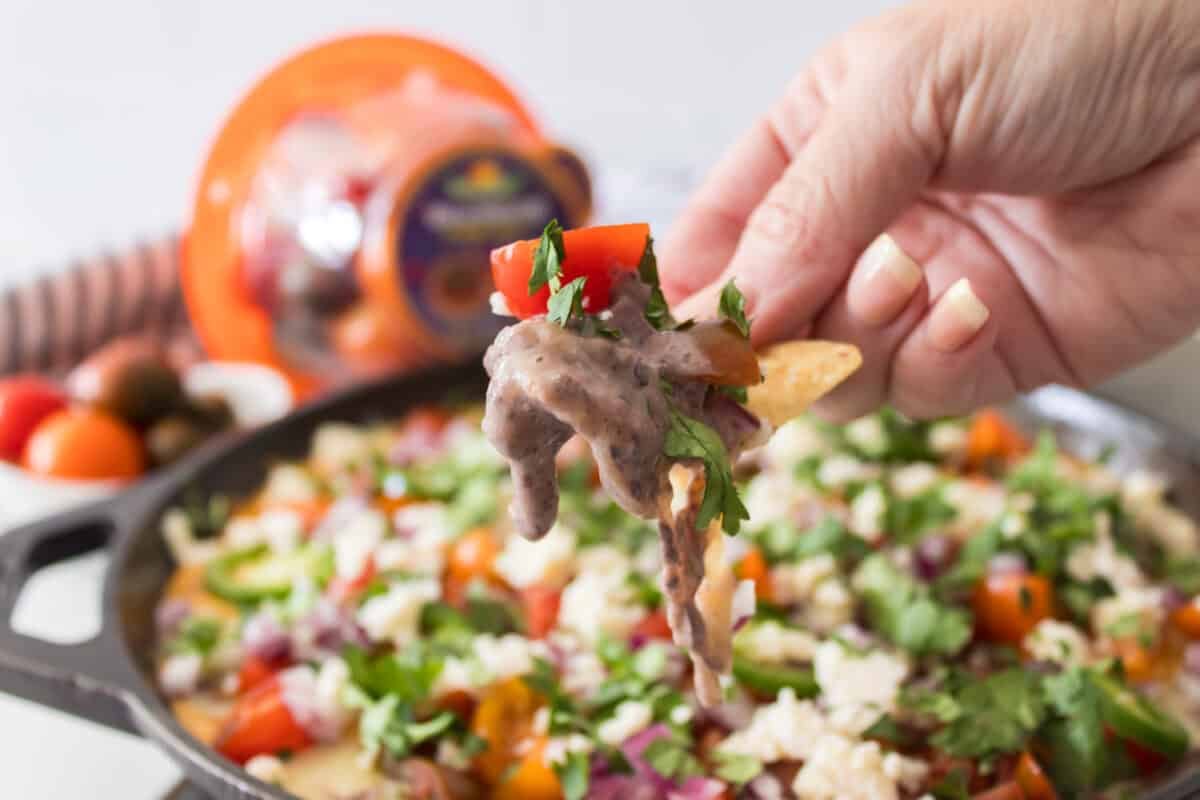 head on shot of hand holding tortilla chip with cheesy black bean dip and cheese pull from skillet