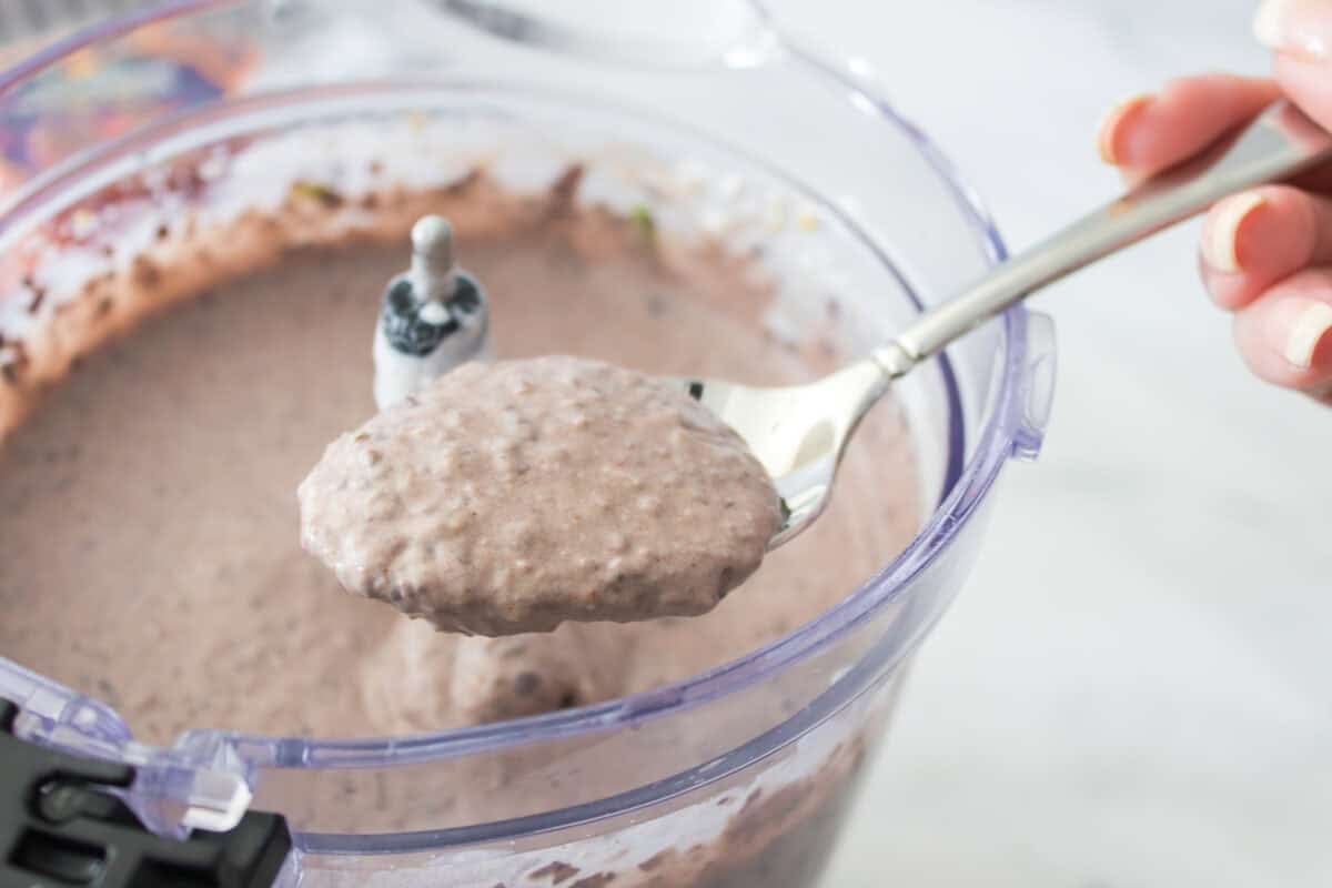 spoon showing thickness and texture of black bean dip over food processor