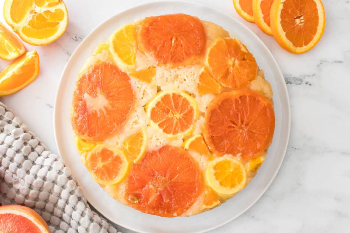 overhead shot of upside down citrus cake on serving plate with slices of oranges and grapefruit surrounding the plate