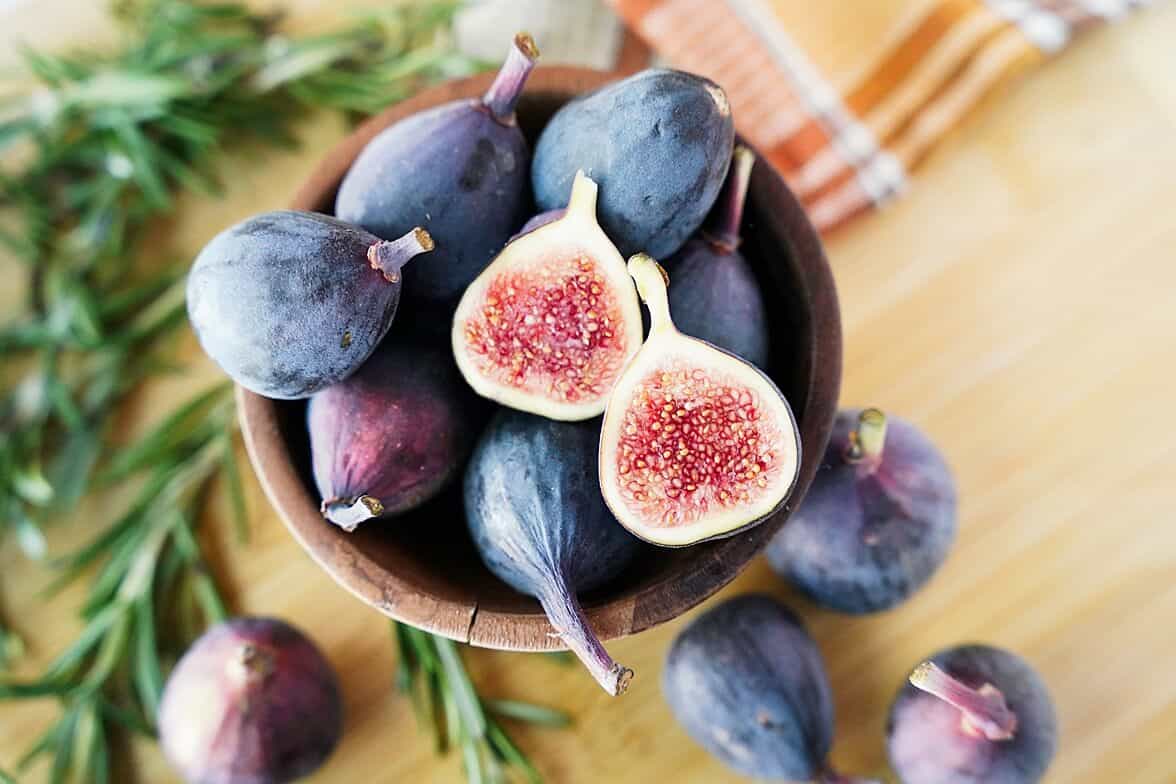 overhead view of figs in a wodden bowl with one fig cut in half