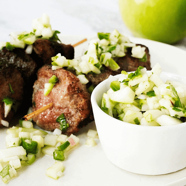 Green apple chimichurri suace in a white bowl next to steak skewers covered in chimichurri sauce