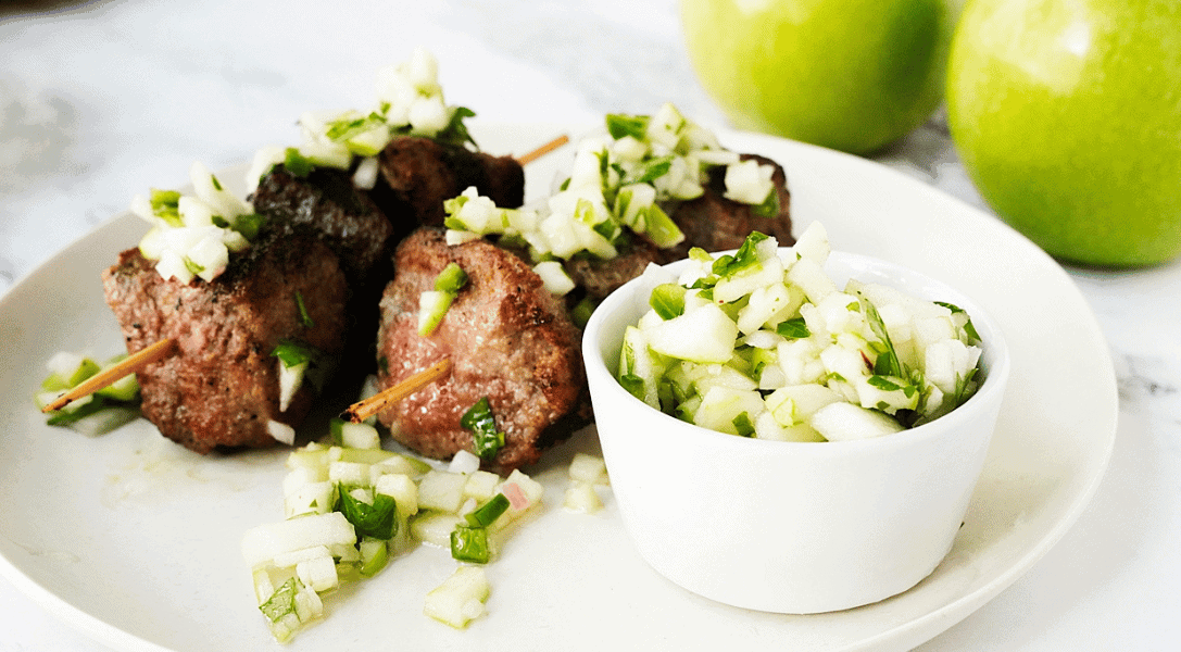 Green apple chimichurri suace in a white bowl next to steak skewers covered in chimichurri sauce