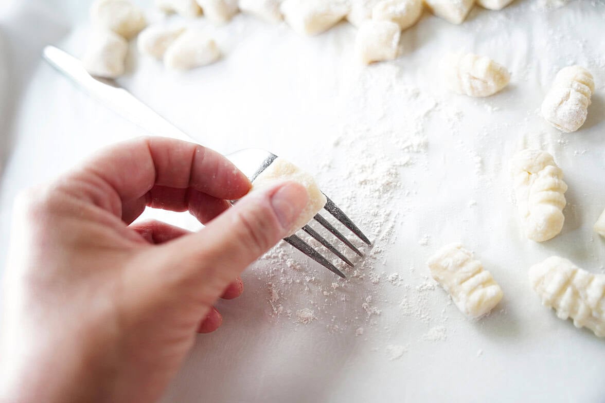 hand holding fork rolling potato gnocchi to make ridges to help hold sauce