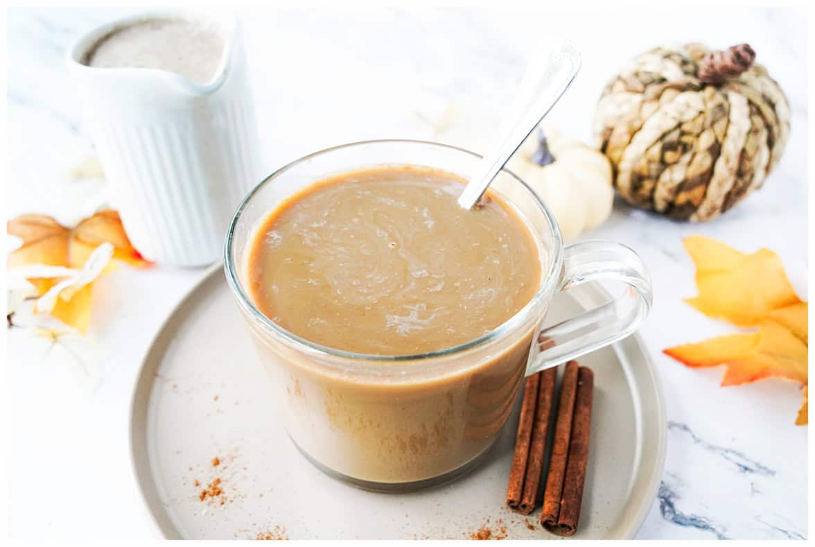 shot of glass coffee mug with coffee and homemade pumpkin spice creamer with spoon on round plate with cinnamon sticks