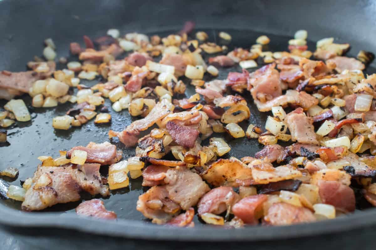 close up shot of crispy bacon and sauteed onions in cast iron skillet