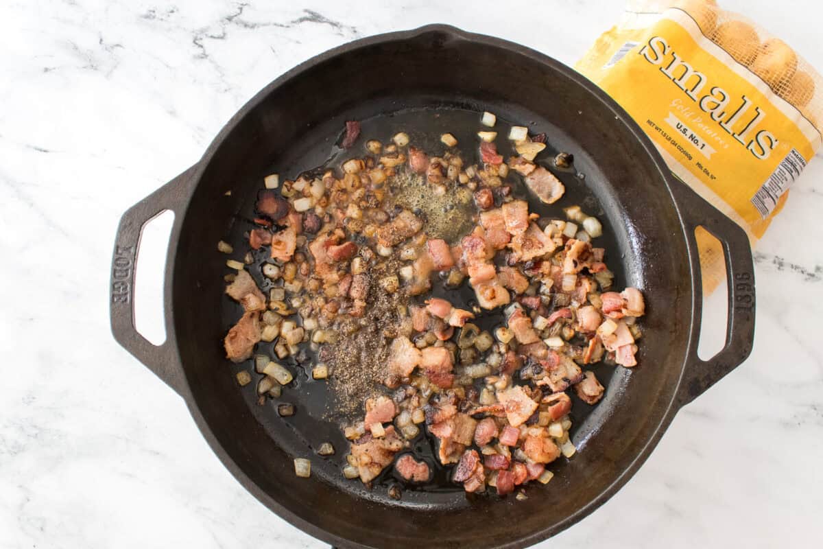 overhead shot of crisp bacon, sauteed onions, salt, pepper, white vinegar, sugar in cast iron skillet