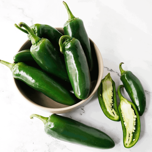Bowl of jalapenos with halved jalapenos for How To Cut Jalapeno Peppers