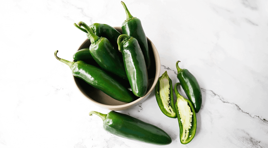 Bowl of jalapenos with halved jalapenos for How To Cut Jalapeno Peppers