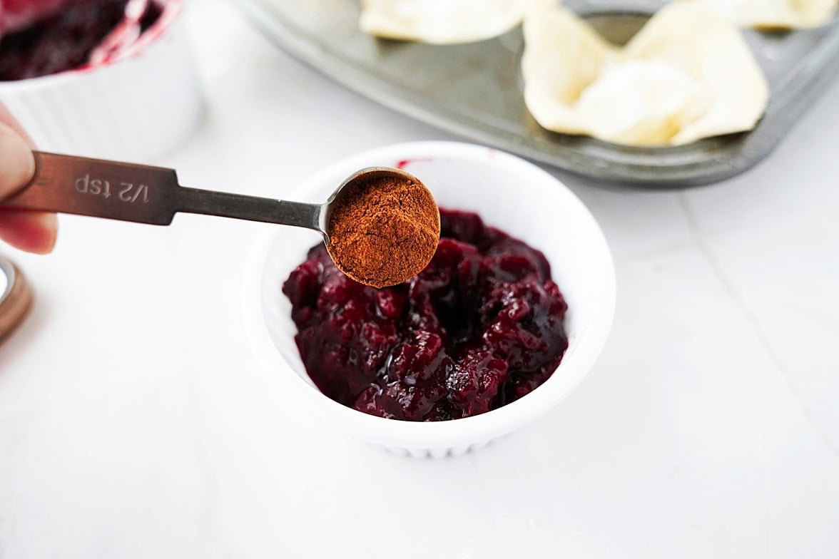 1/2 tsp of cinnamon being added to 1 cup of jelly in white bowl