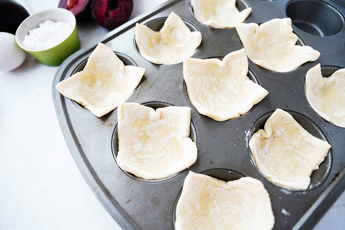 muffin tin with 9 pieces of puff pastry, one slice of puff pastry in each tin