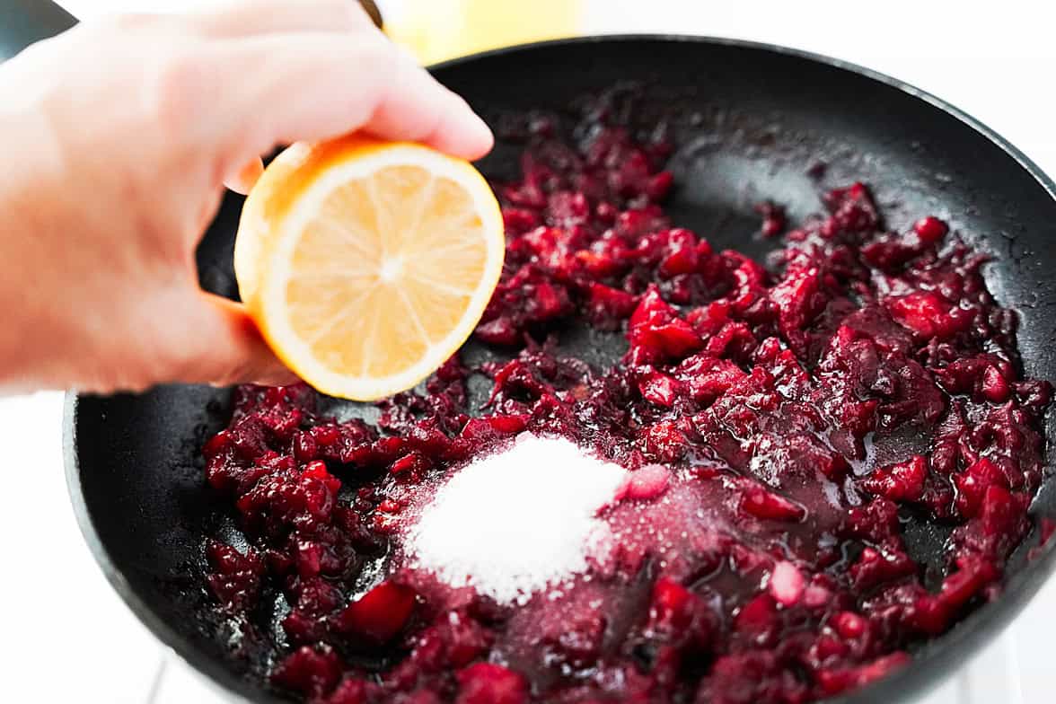 hand squeezing a half of a lemon over skillet with plums and water that have been cooked down and sugar