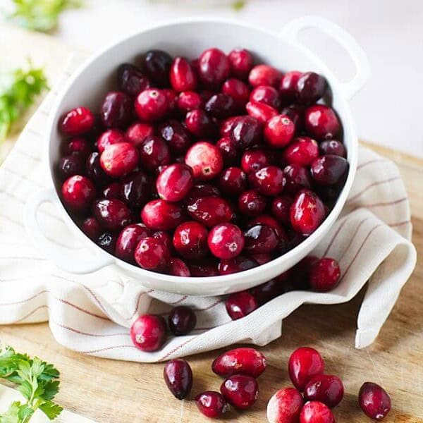 Close up of fresh cranberries in white bowl surrounded by herbs