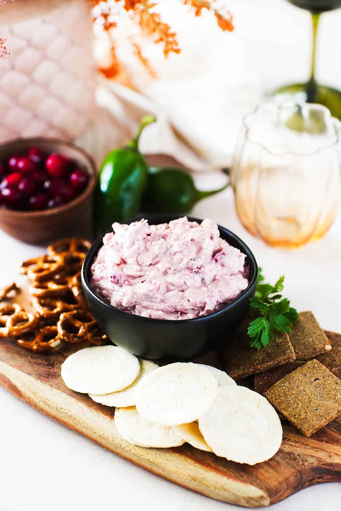 vertical head on shot of cranberry jalapeno dip in black bowl sitting on wooden serving platter with pretzels and crackers