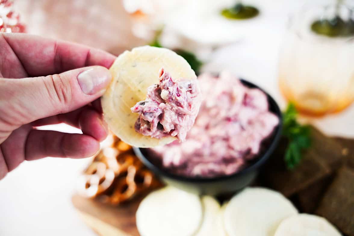 hand holding cracker with a scoop of cranberry jalapeno dip with dip in black bowl in background