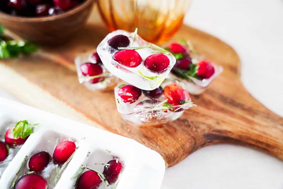 Cranbery ice cubes on a wooden board with ice cube tray in the front