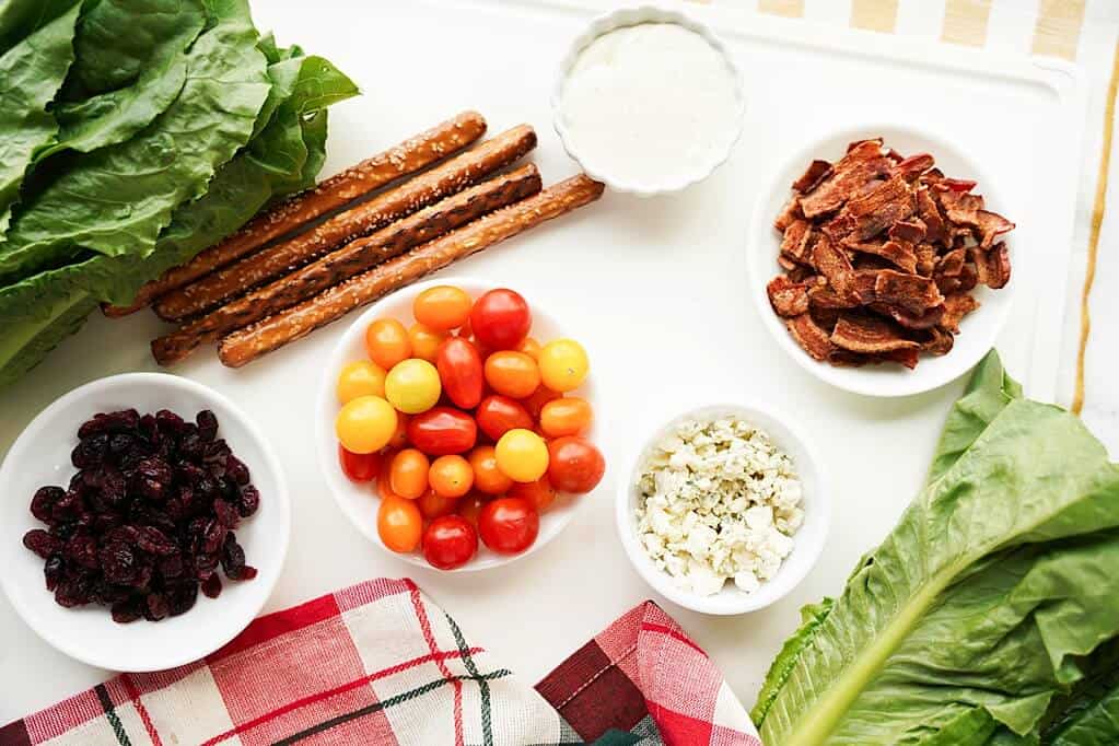 Ingredients for Christmas Tree Salad Board: romaine, grape tomatoes, dried cranberreis, blue cheese, bacon, pretzel rods and dressing