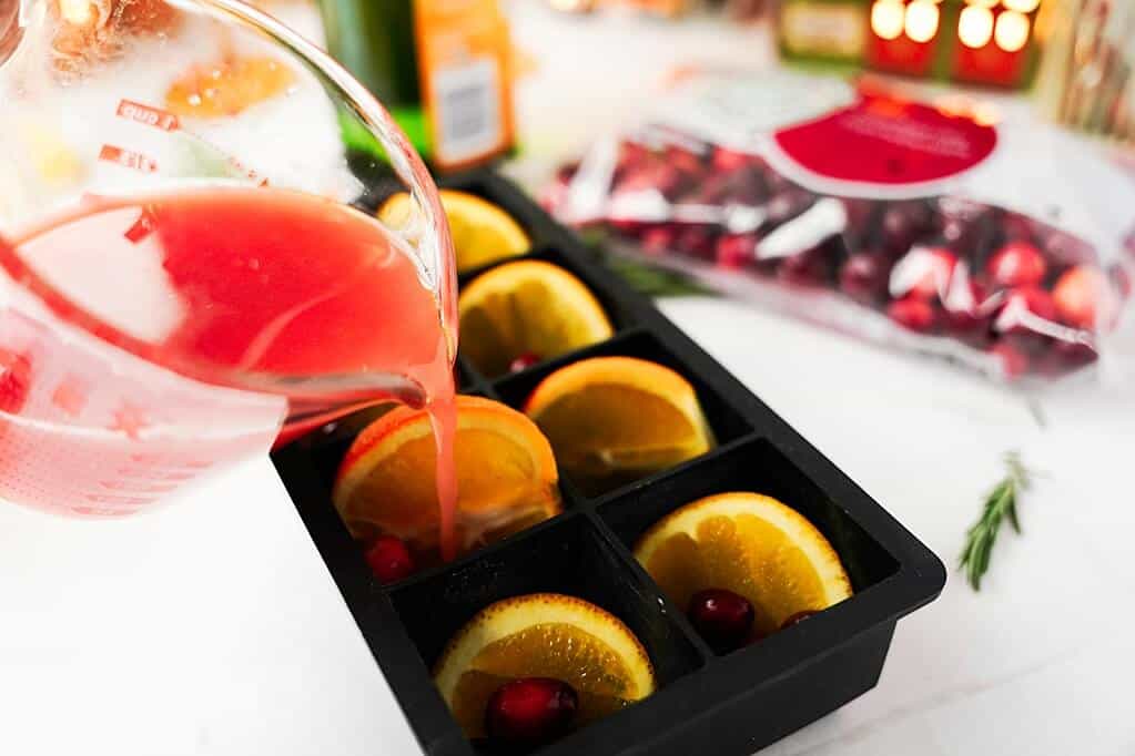 pouring orange/cranberry juice mixture into the ice cube molds