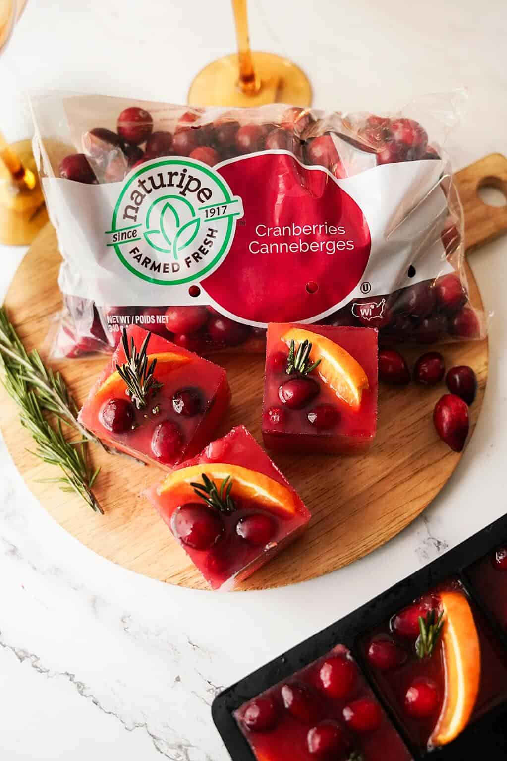 Cranberry, orange and rosemary ice cubes on a board with a bag of Naturipe cranberries