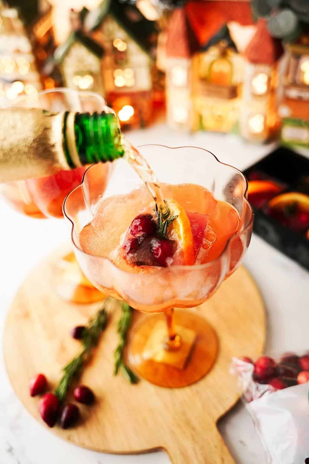 Vertical image of pouring champagne into glass with cranberry/orange/rosemary ice cube