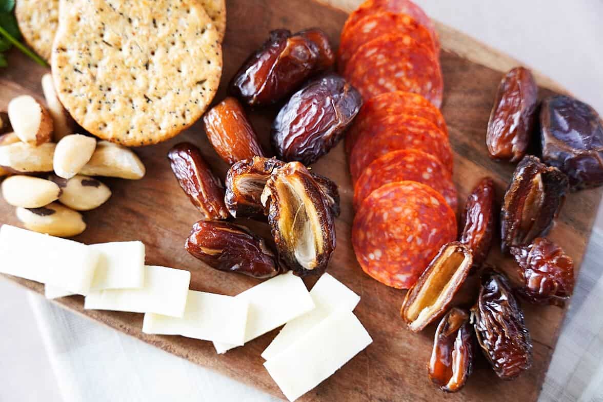 Dates ona. charcuterie board with crackers, cheese, nuts and pepperoni