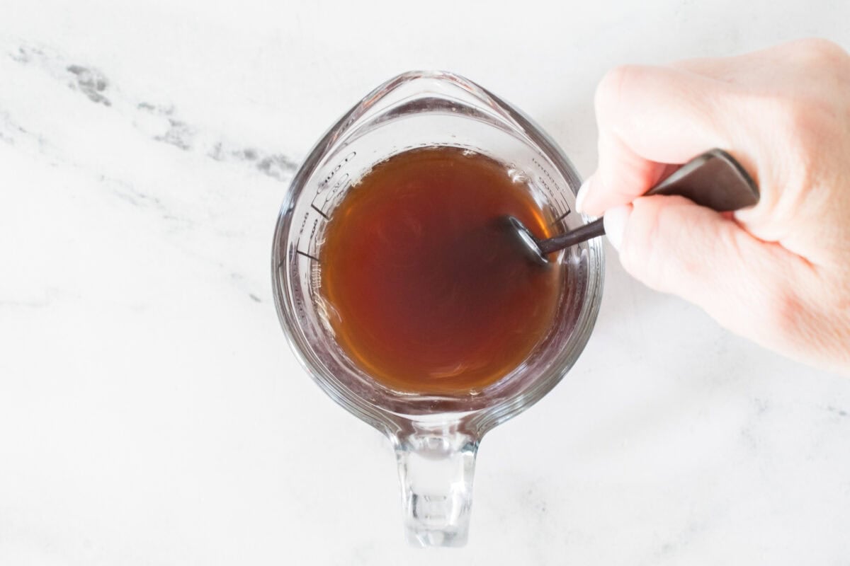 glass measuring cup with hand mixing chicken stock, soy sauce, rice vinegar and brown sugar