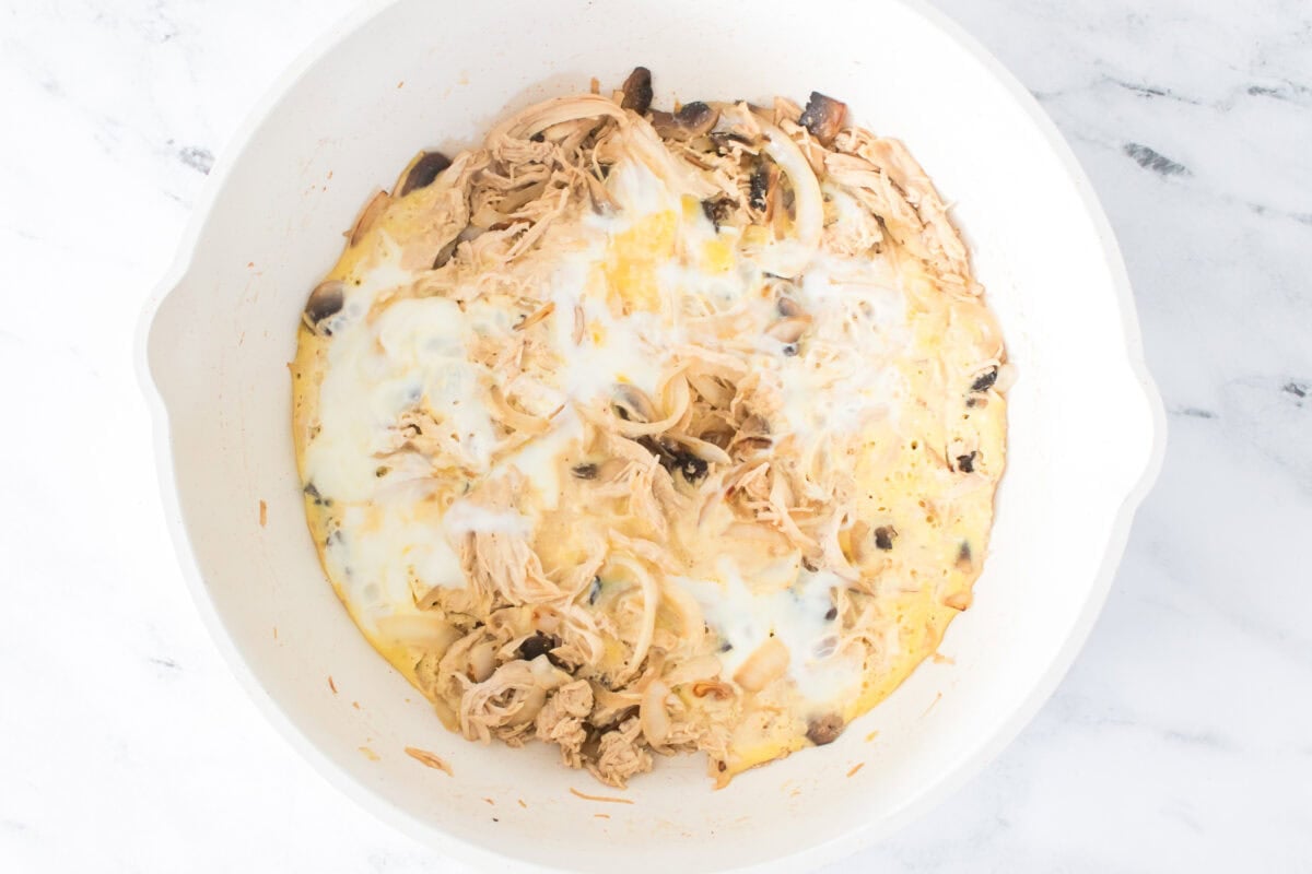 over head shot of overhead shot of oil, shredded chicken, sliced mushrooms, sliced onions and brown sugar soy sauce with eggs that have set in white wok