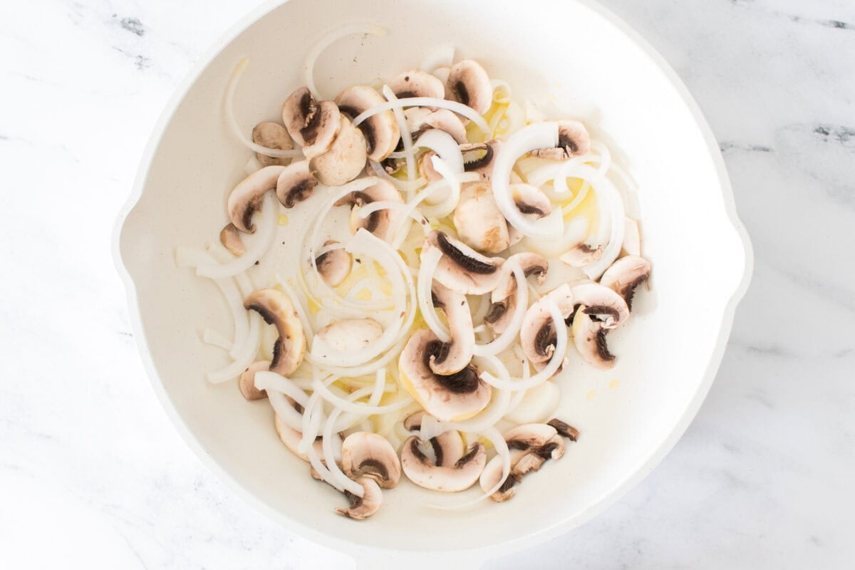 overhead shot of oil, sliced onions and mushrooms in white wok