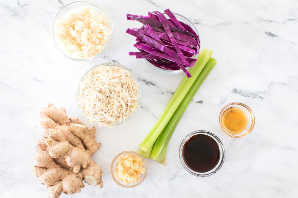 ingredients to make egg roll in a bowl: white rice, sliced red cabbage, shredded chicken, fresh ginger, celery sticks, minced garlic, soy sauce and sesame oil