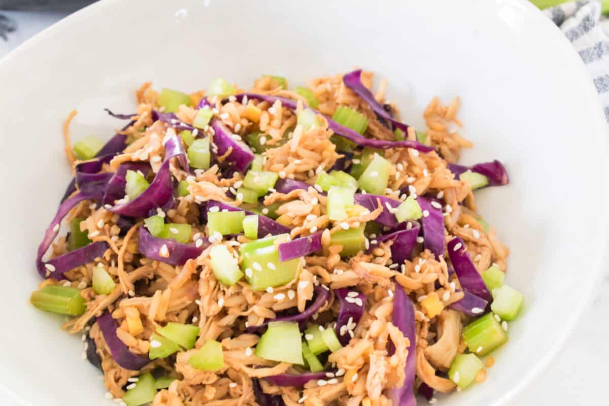 close up shot of egg roll in a white bowl topped with chopped celery and sesame seeds