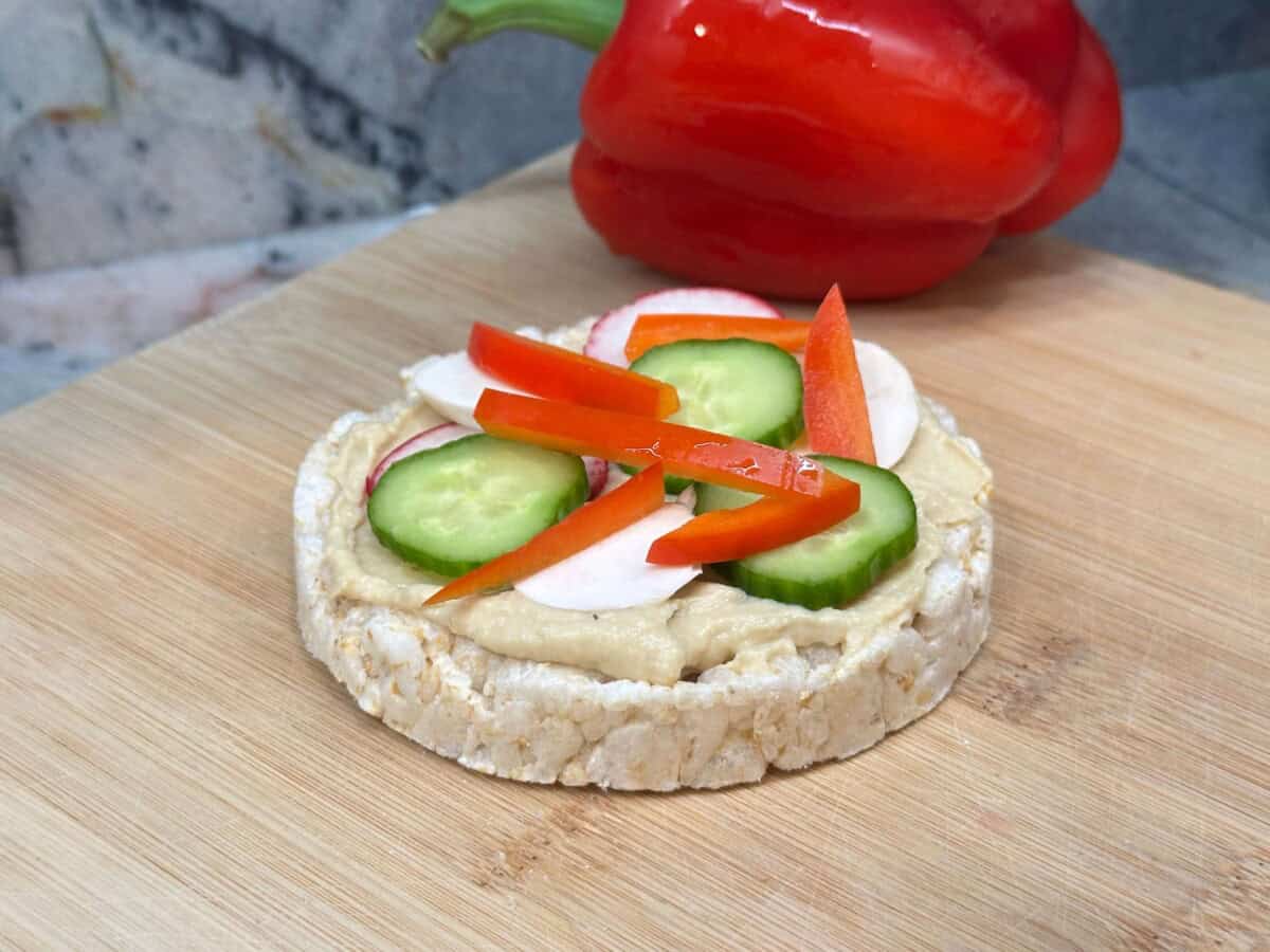side view of a veggie rice cake pizza on a wood cutting board