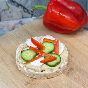 Vertical image of veggie rice cake pizza on a wood cutting board