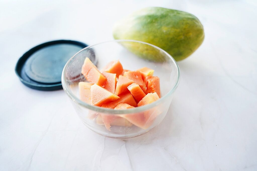 Cut papaya in a glass container with lid and whole papaya next to it