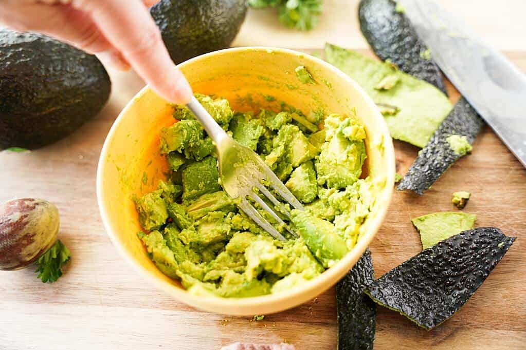 Mashed avocado in yellow bowl with fork