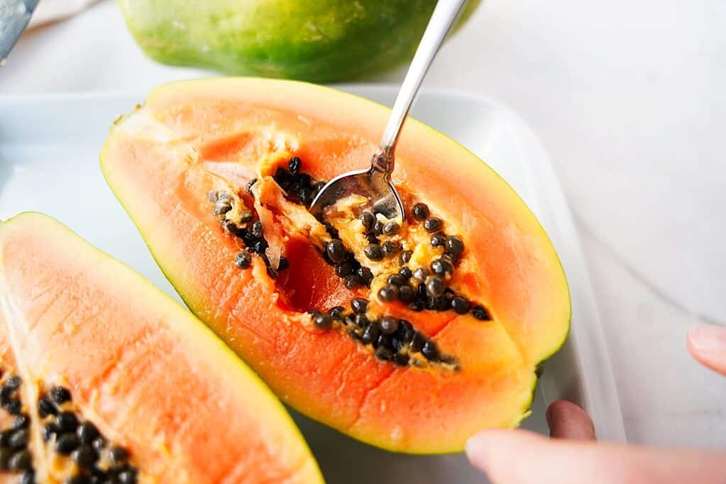 Silver spoon scooping out the seeds of a papaya