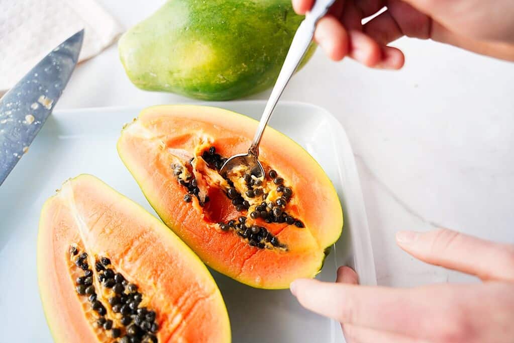 silver spoon scooping out the seeds of a papaya