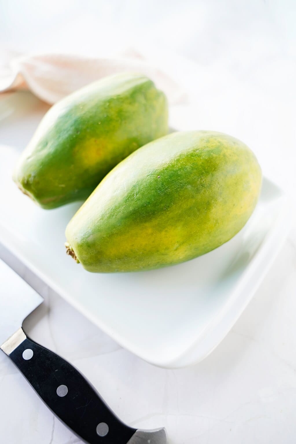 Vertical image of 2 papayas on a white plate with a knife to the side