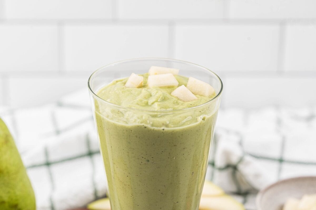 Blended green goddess smoothie in a glass and topped with diced pear to serve.