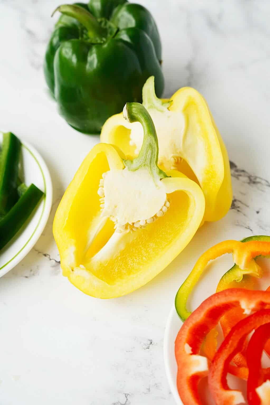vertical image of cut yellow bell pepper, green whole pepper and some pepper rings