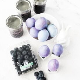 Vertical image of blueberry-dyed hard boiled eggs with jars of blueberry juice and North Bay Produce blueberries