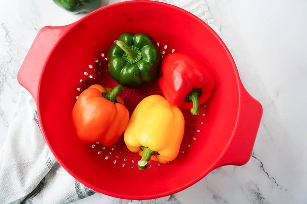 red, green, orange and yellow bell pepper in red strainer before getting washed