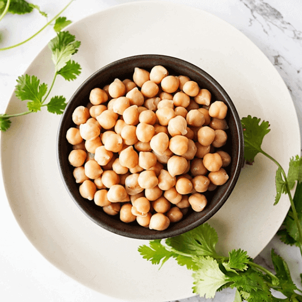 overhead view of chickpeas in a black bowl on a white plate with subtle parsley