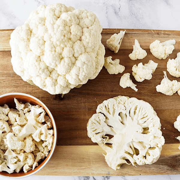 Head of cauliflower, cauliflower florets and cauliflower steak on wood cutting board