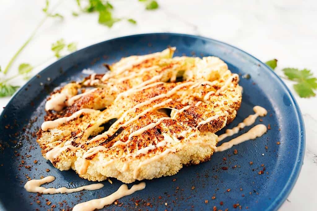 Cooked Cauliflower steak on a blue plate with dressing on top