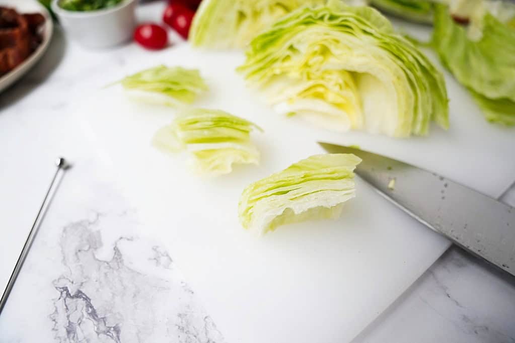 Cut wedge salad pieces on a cutting board with a knife.