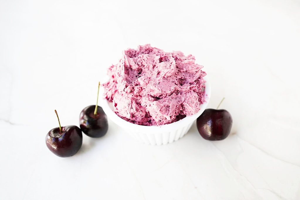 Cherry buttercream frosting in a ramekin with fresh cherries.